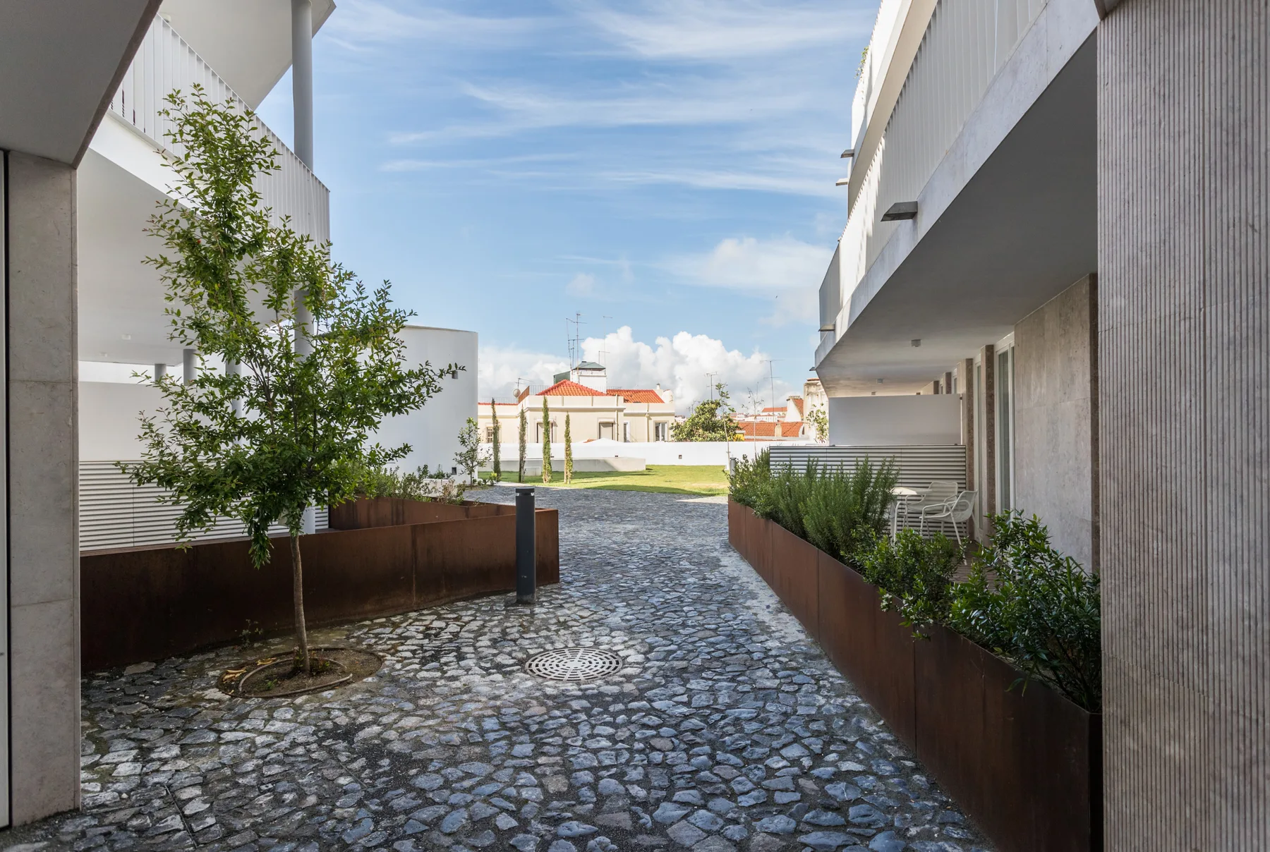 A paved courtyard between modern buildings, with raised planters and outdoor seating.