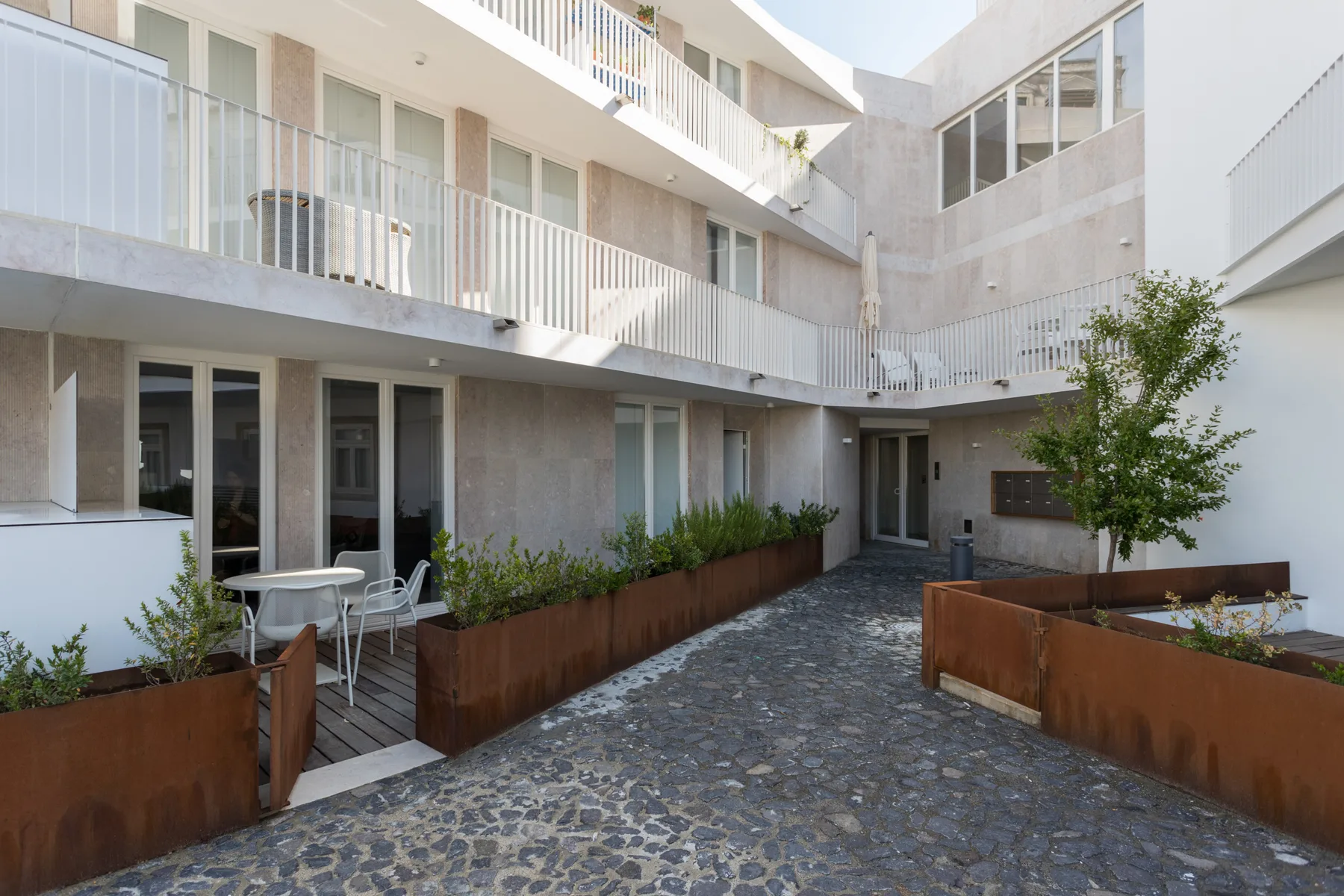 A paved courtyard with planted raised beds and outdoor seating beside a modern building.