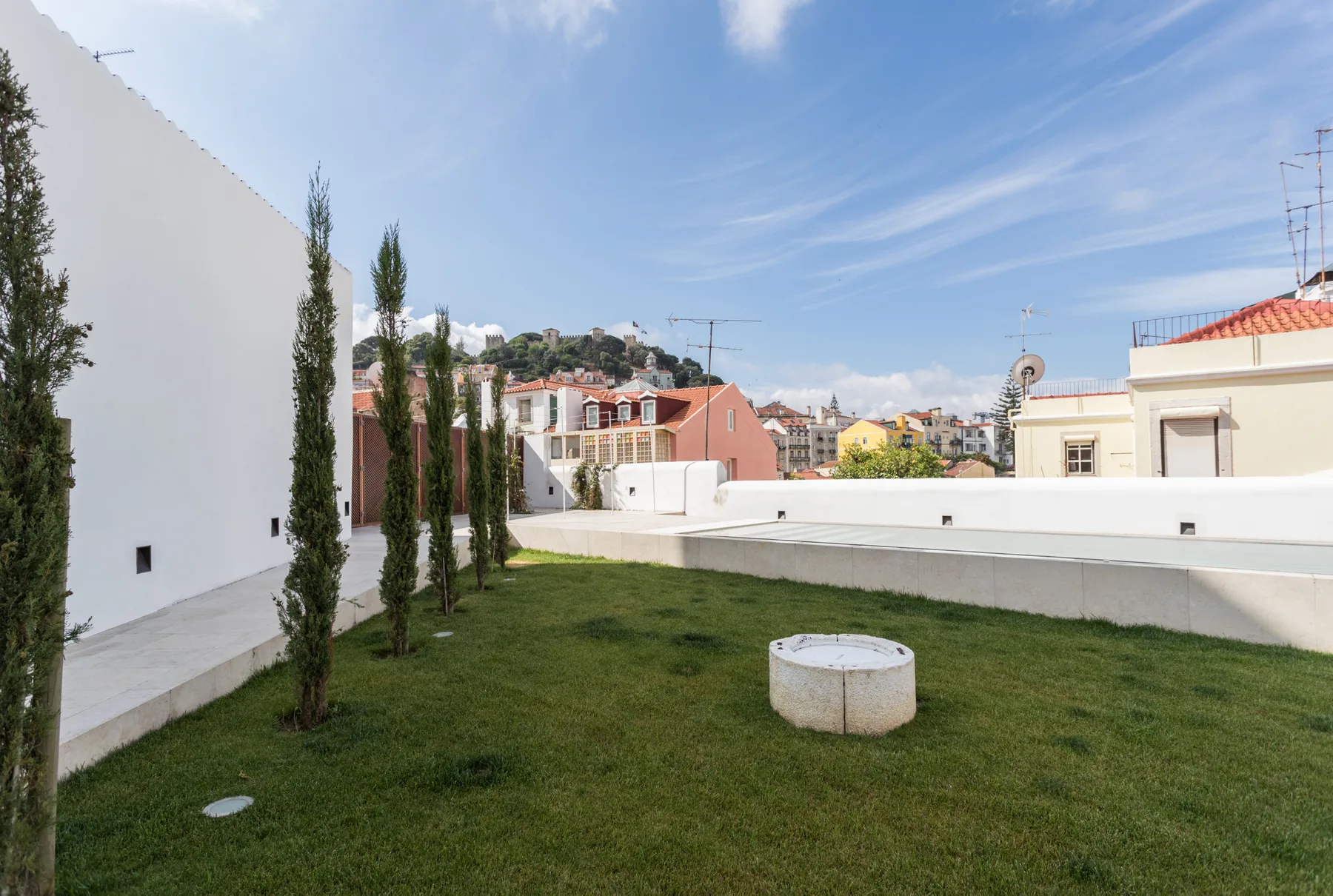 A grassy rooftop terrace with a low circular feature and neighboring rooftops beyond.