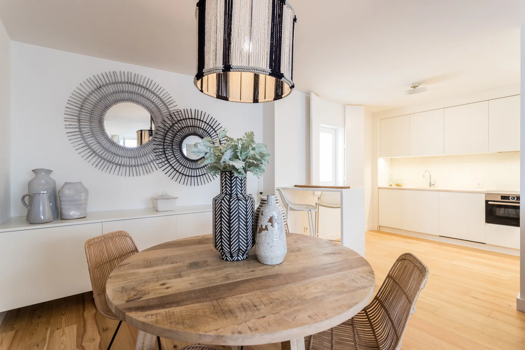 A dining area with a round wooden table beside a bright kitchen.