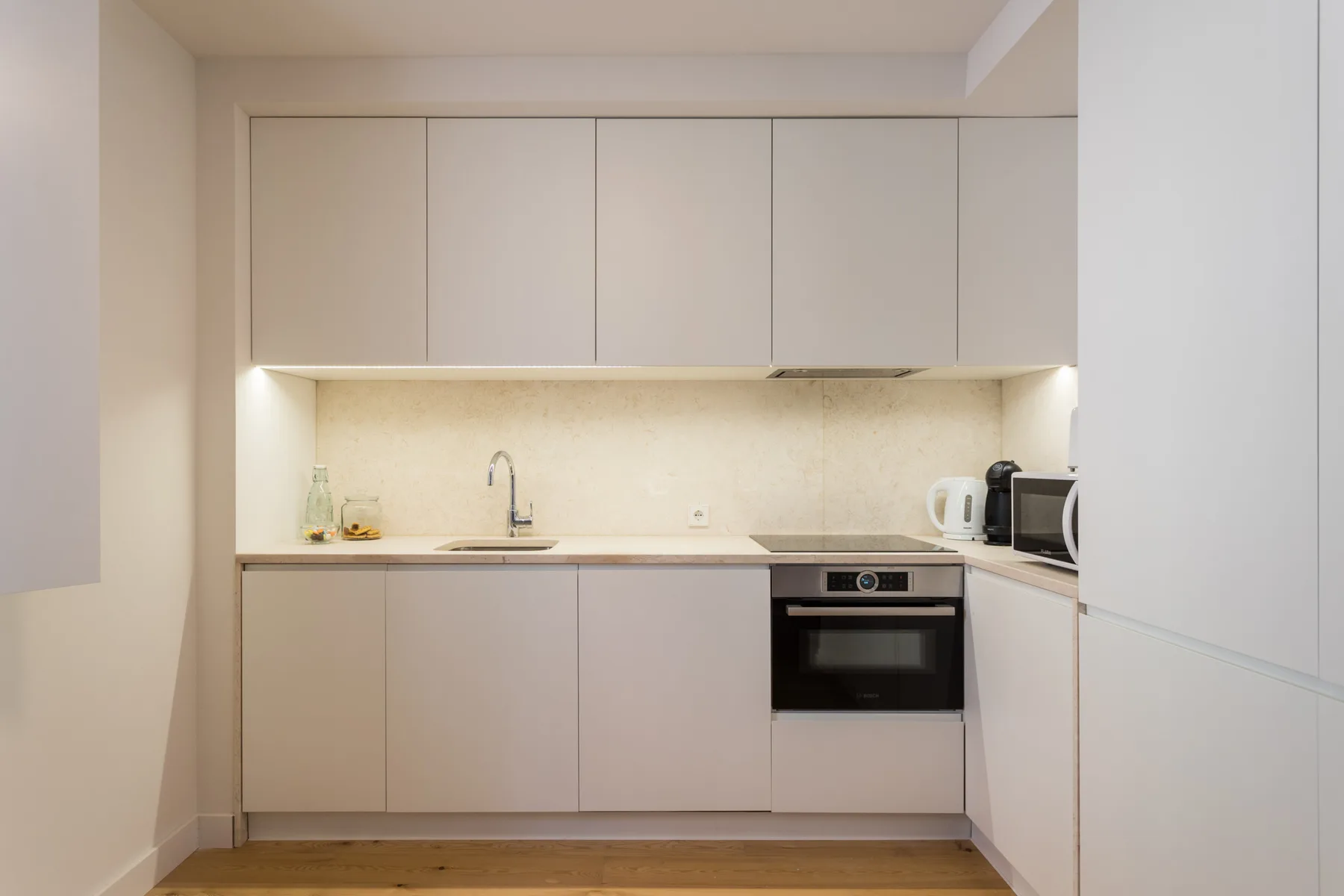A modern kitchen with pale cabinets, a countertop, and built-in appliances.
