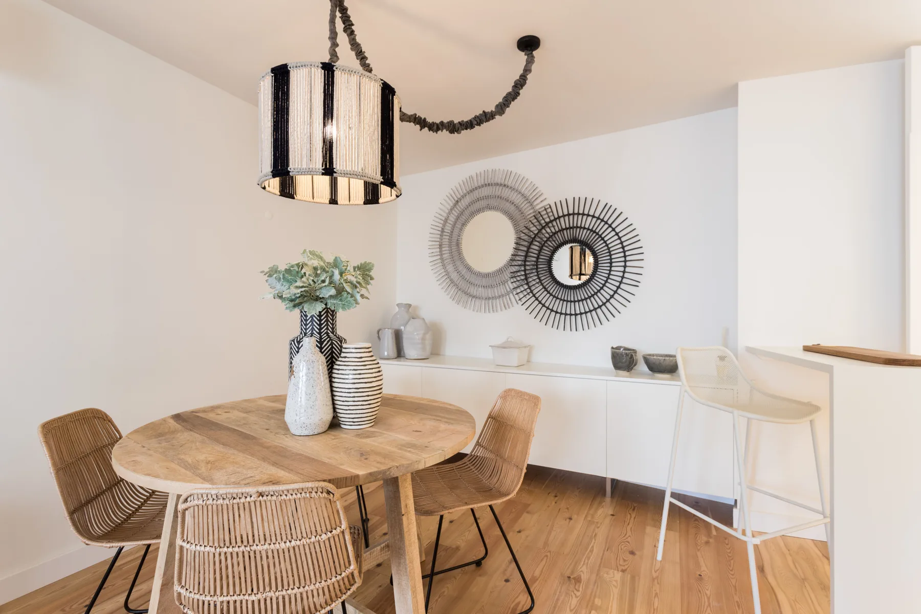A dining area with a round wooden table, woven seating, and wall mirrors.