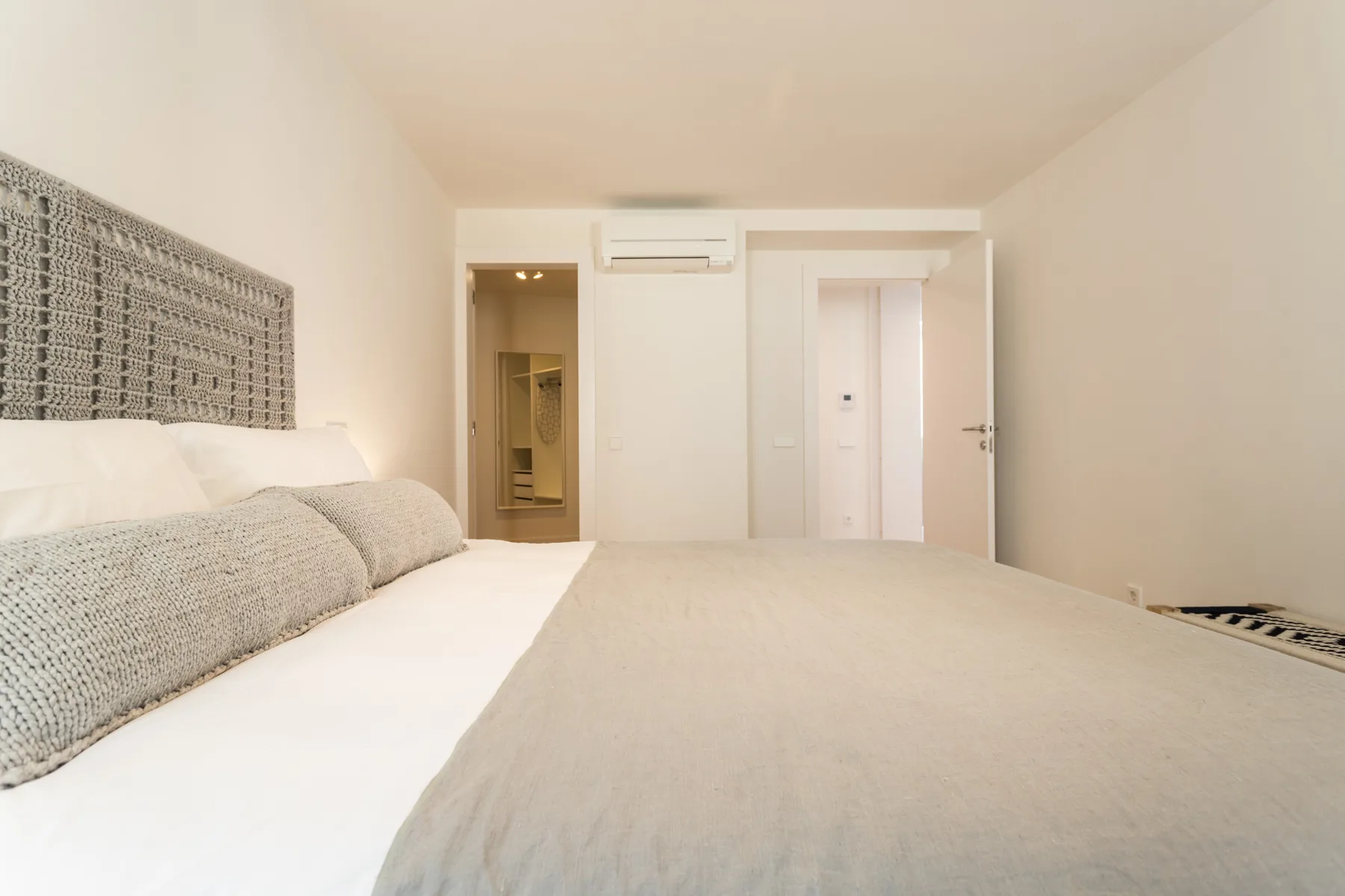 Dormitorio con cama, cabecero texturizado y una puerta hacia el baño.