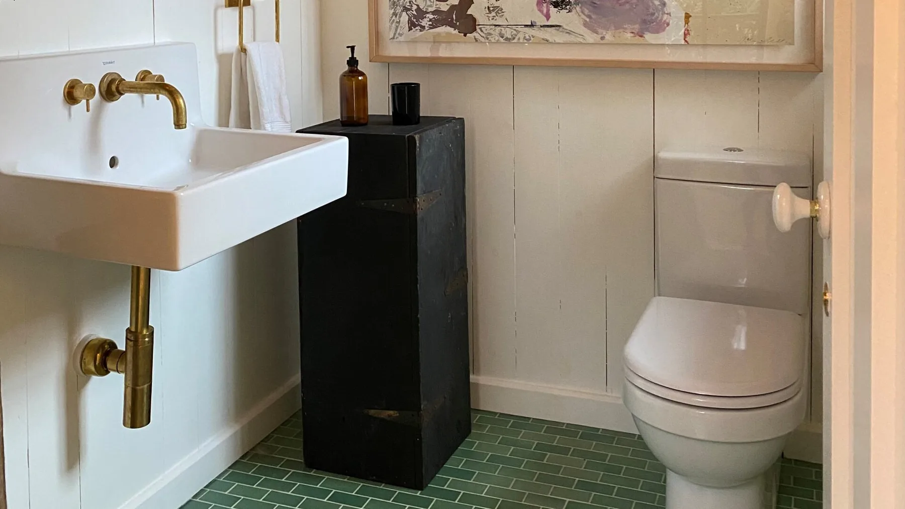 A bathroom with a wall-mounted sink, toilet, and dark cabinet.