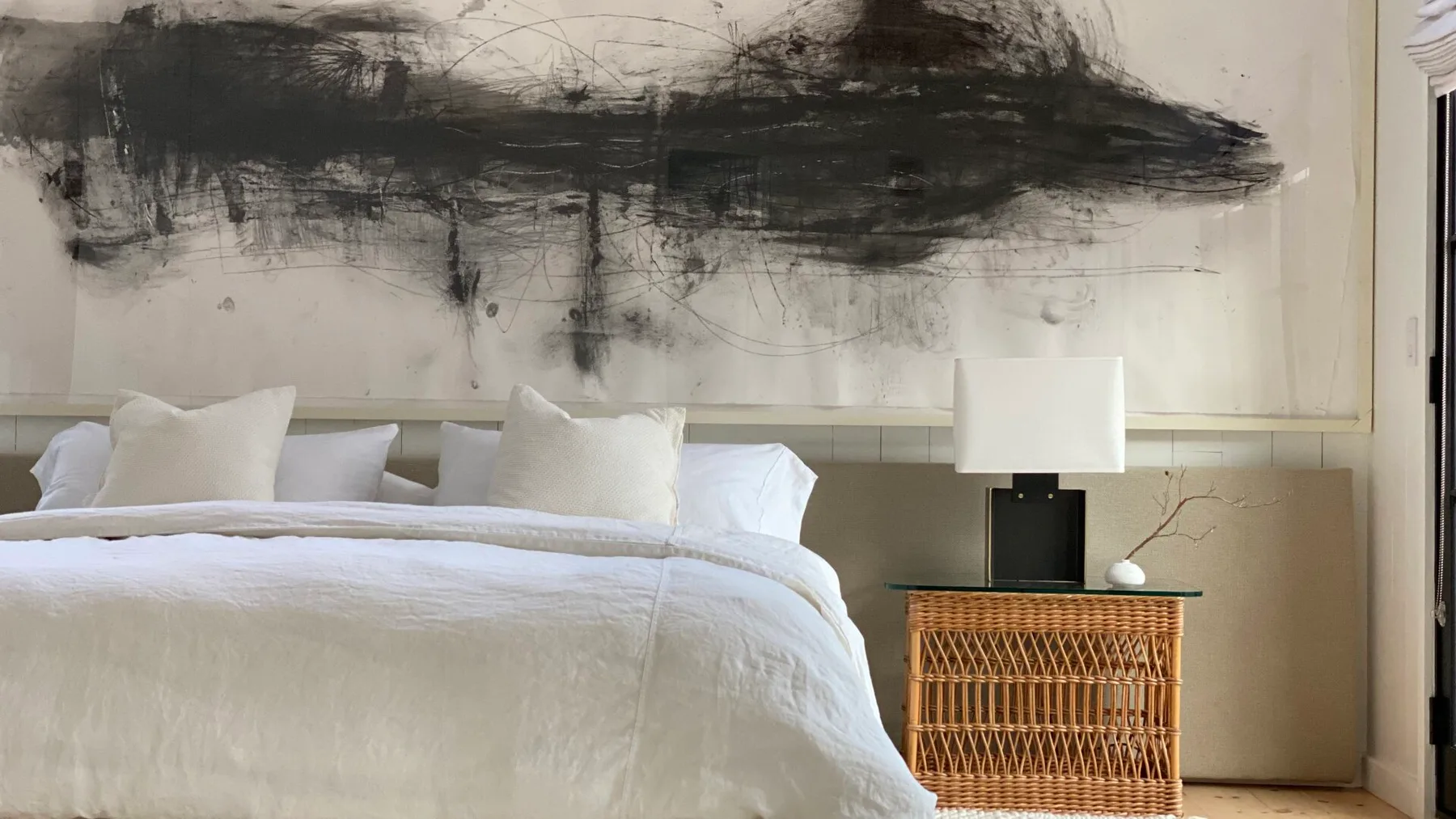 A bedroom with a neatly made bed, bedside table, and large abstract artwork.