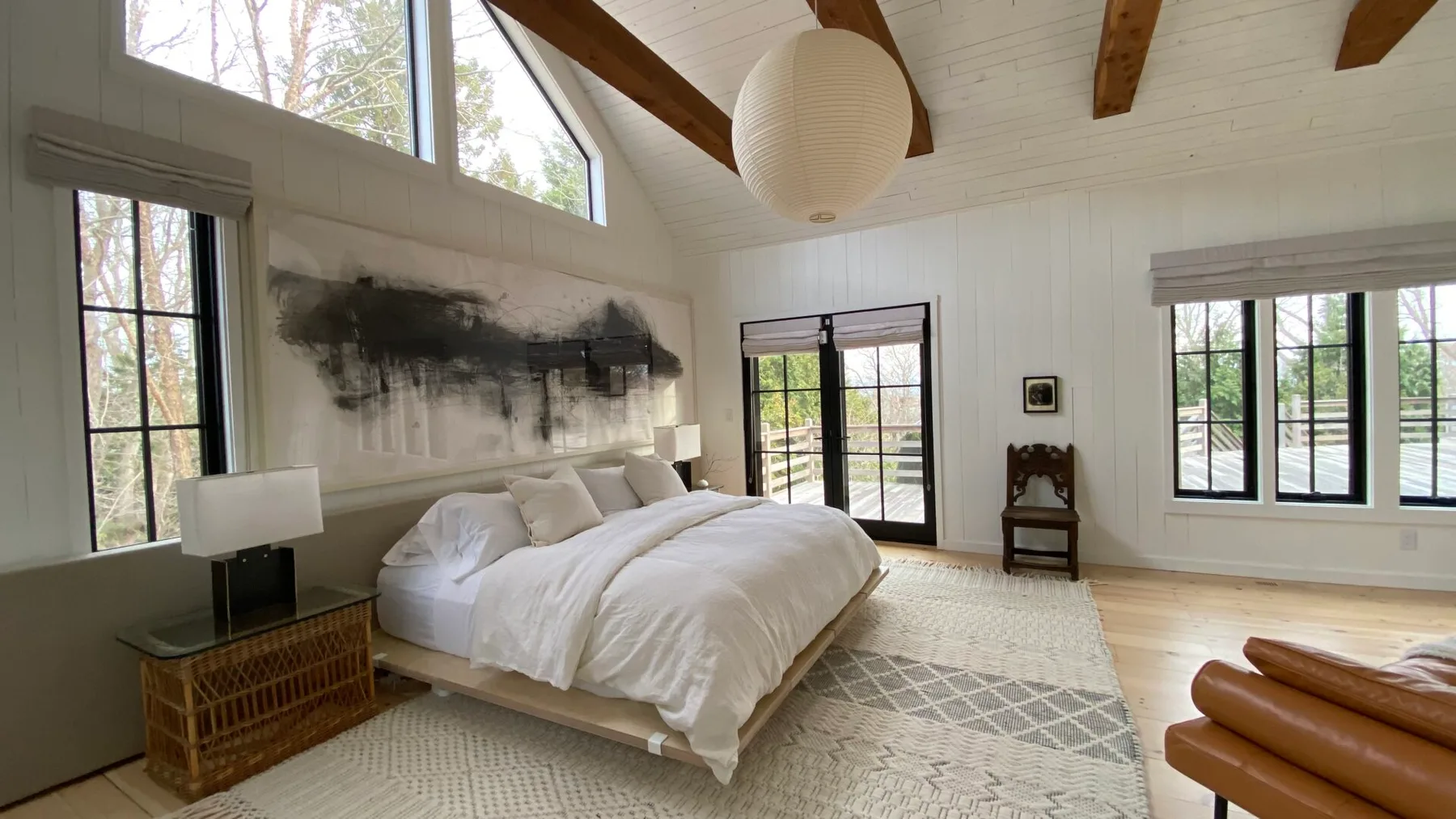 A bright bedroom with a white bed, tall windows, and exposed ceiling beams.