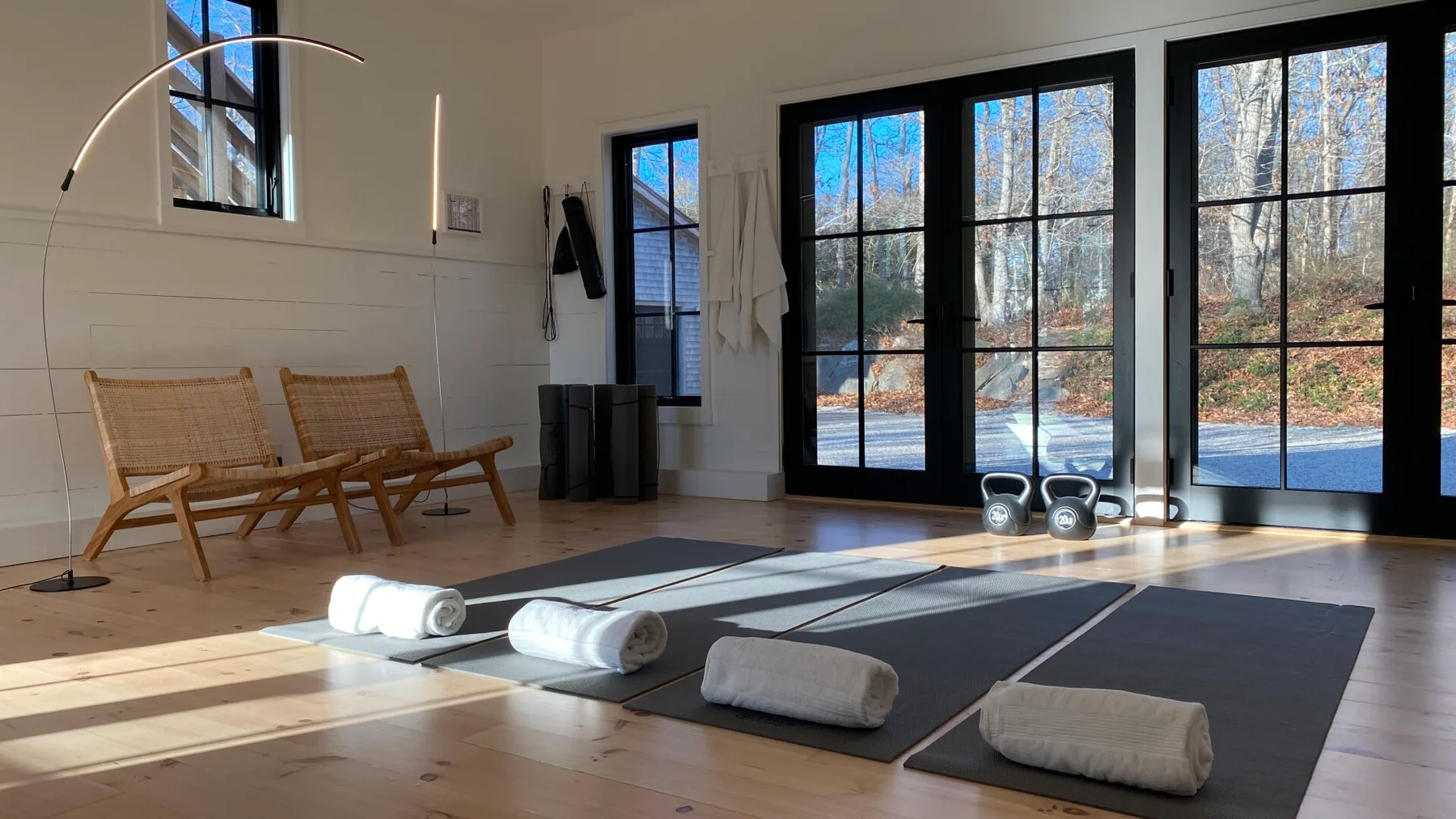 A bright exercise room has floor mats, rolled towels, and large windows.