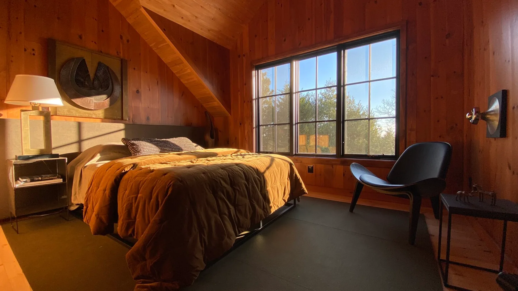 A wood-paneled bedroom with a bed beside a large window and seating.