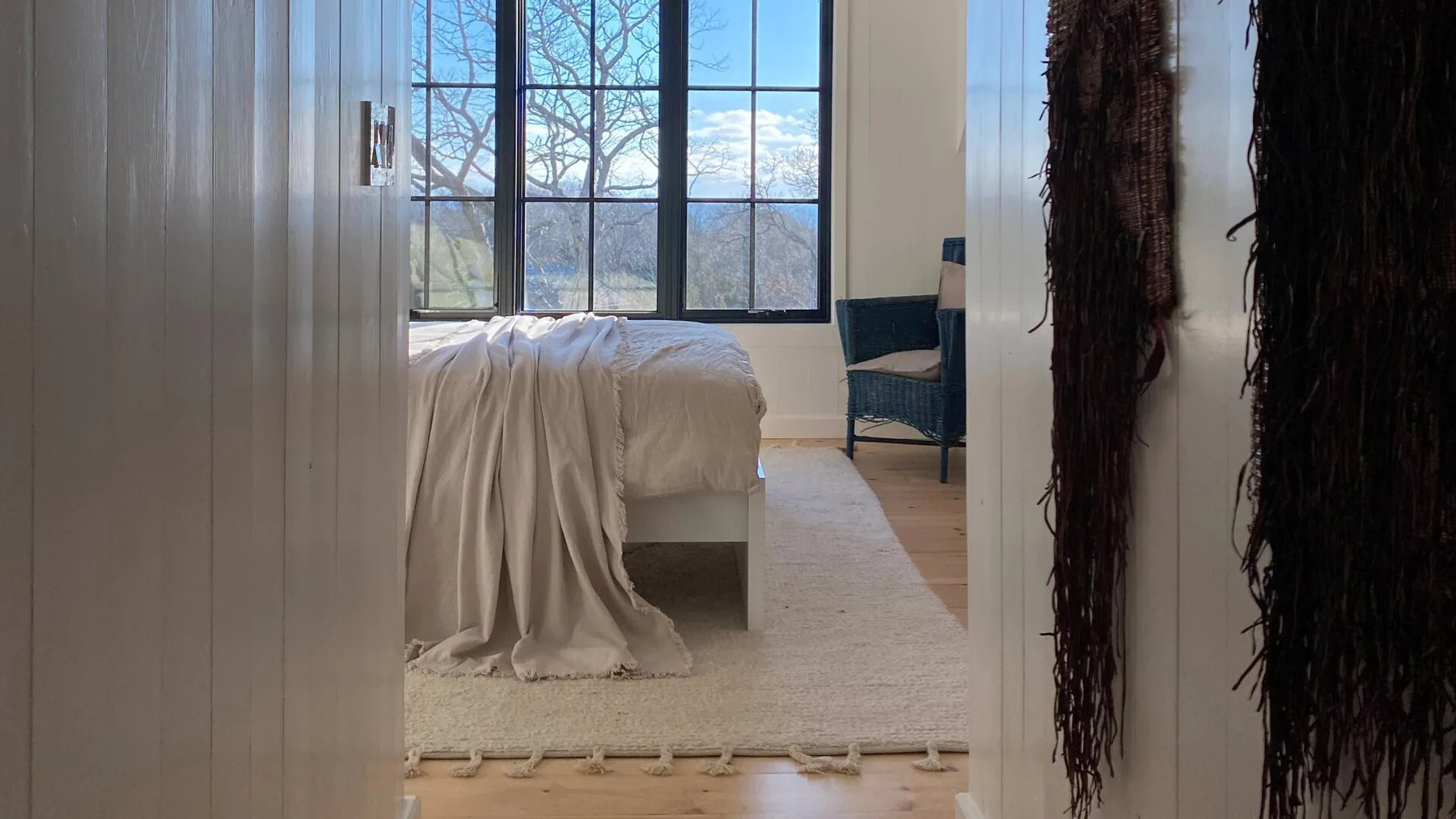 A bedroom with a bed beside a large window overlooking a wooded landscape.