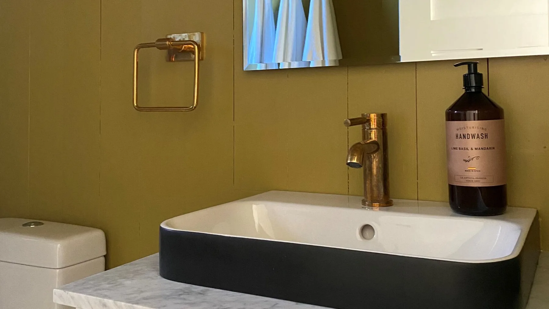 A bathroom vanity with a white basin, dark sink base, and brass faucet.