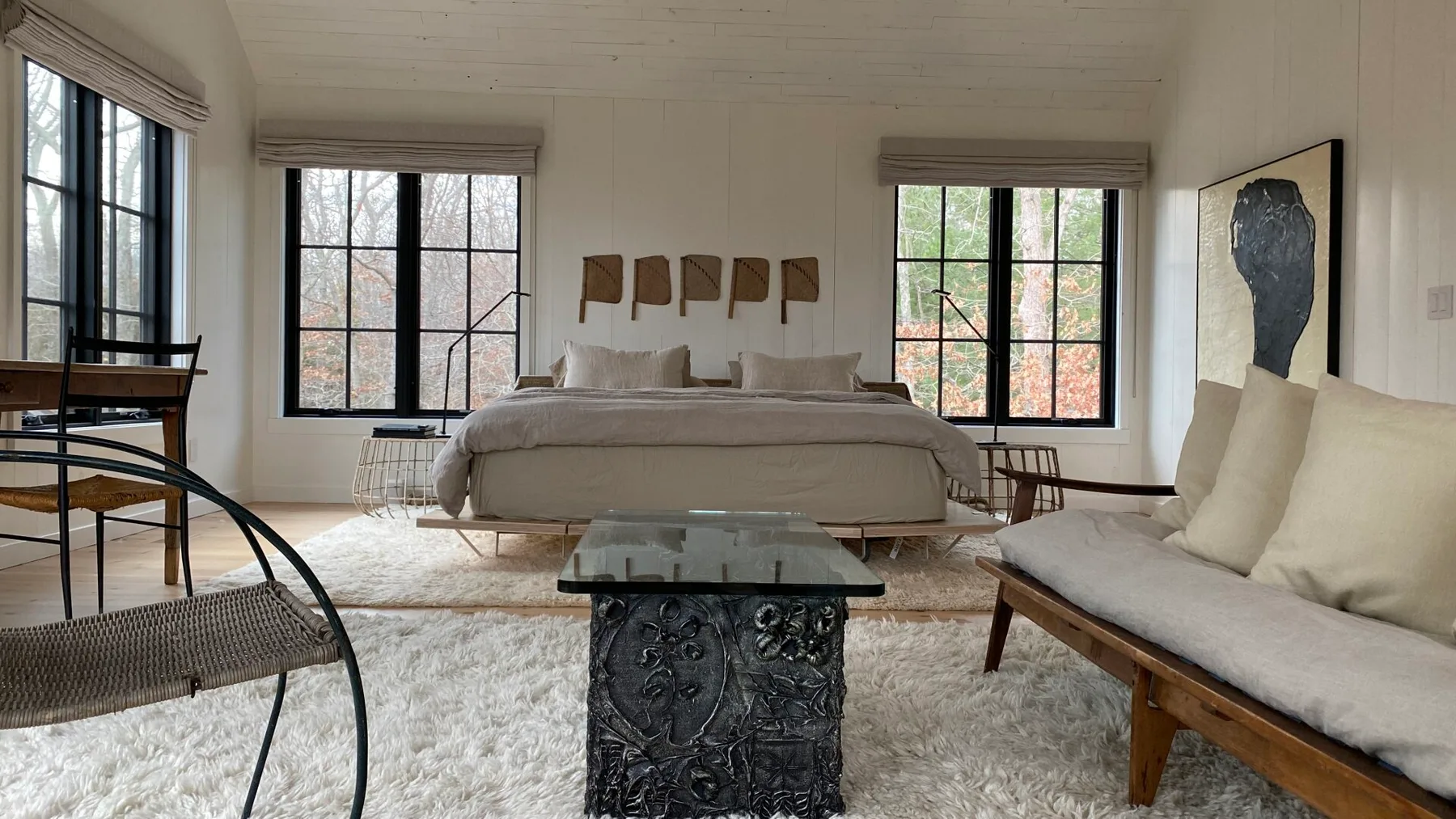 A bright bedroom with a large bed, broad windows, and a seating area.
