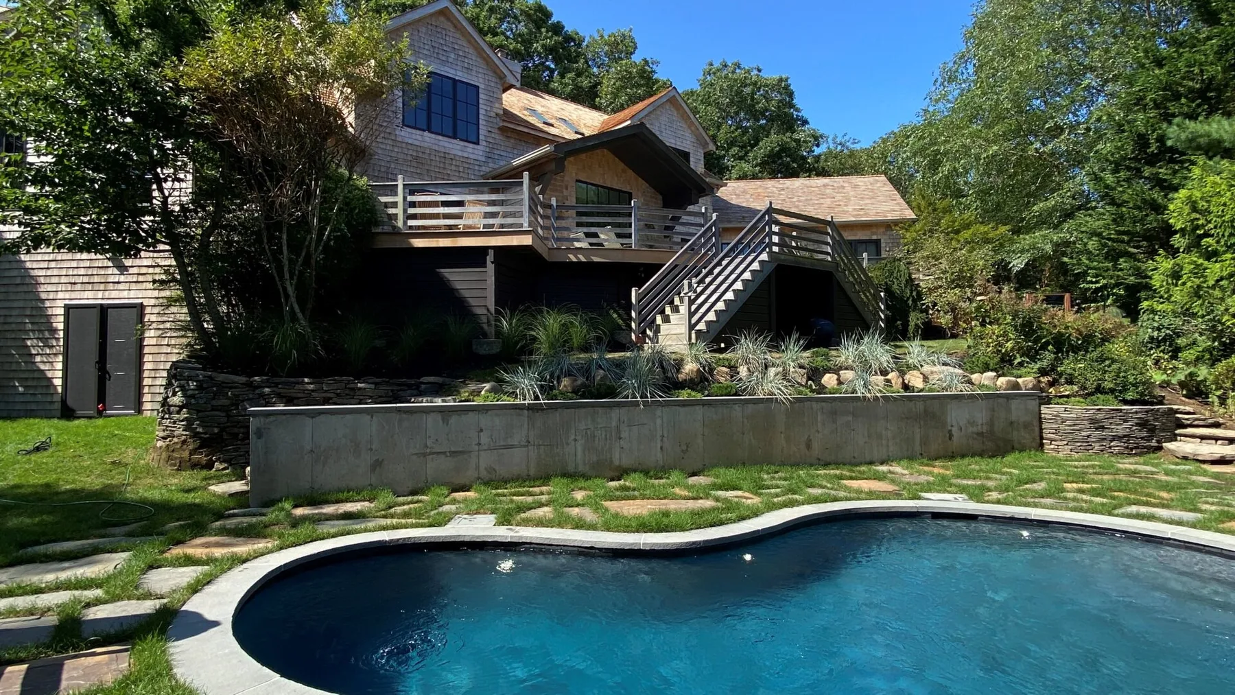 A house overlooks a swimming pool, with landscaped stone paths and greenery.