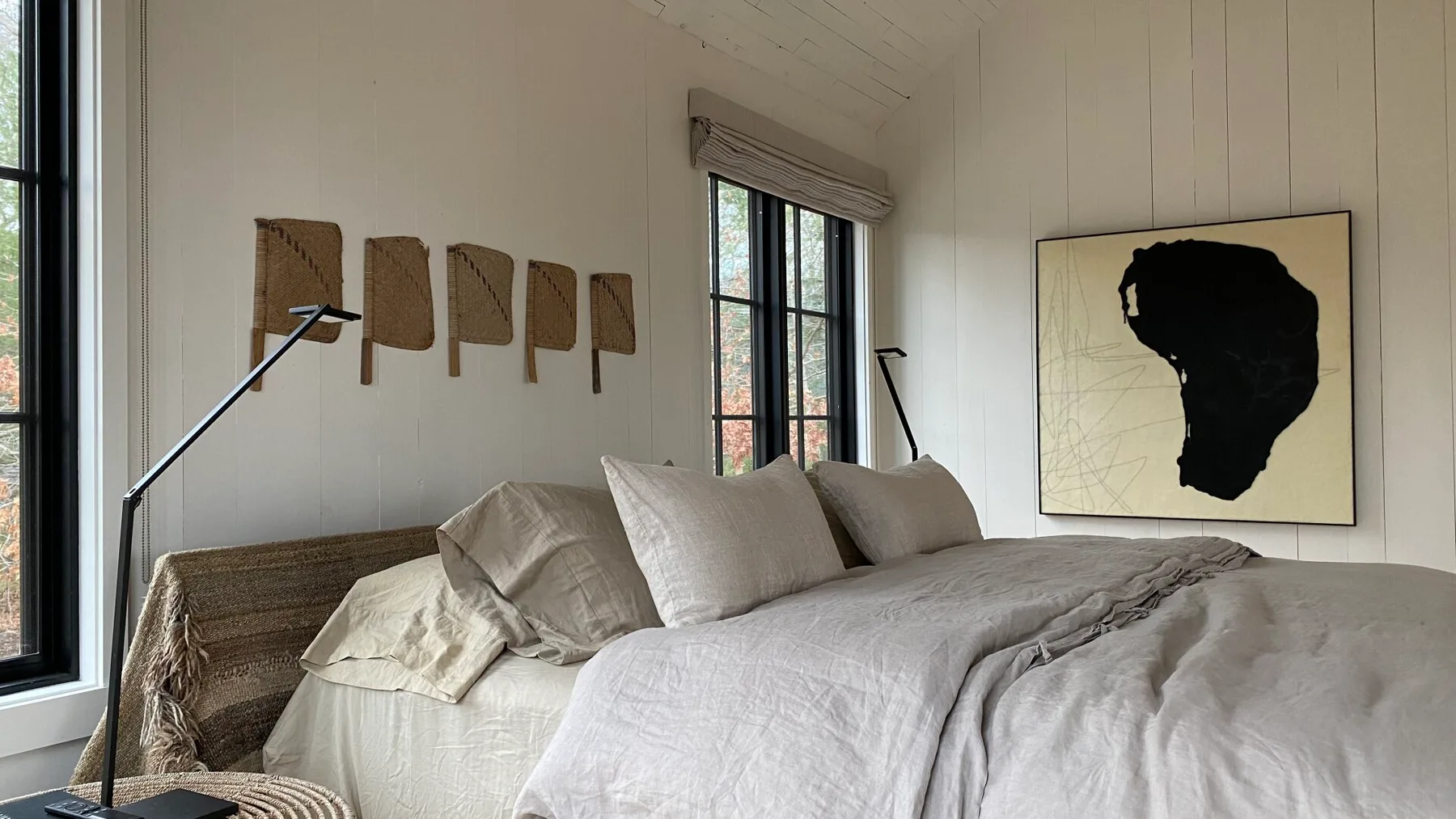 A bright bedroom with a large bed, tall windows, and framed wall art.