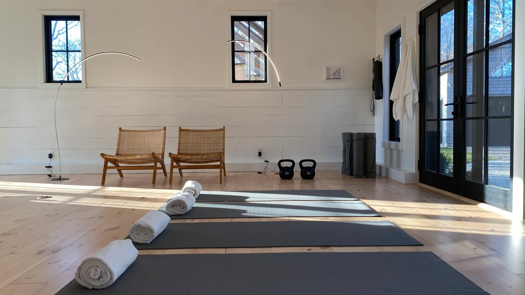 A bright exercise room with yoga mats and chairs by the windows.