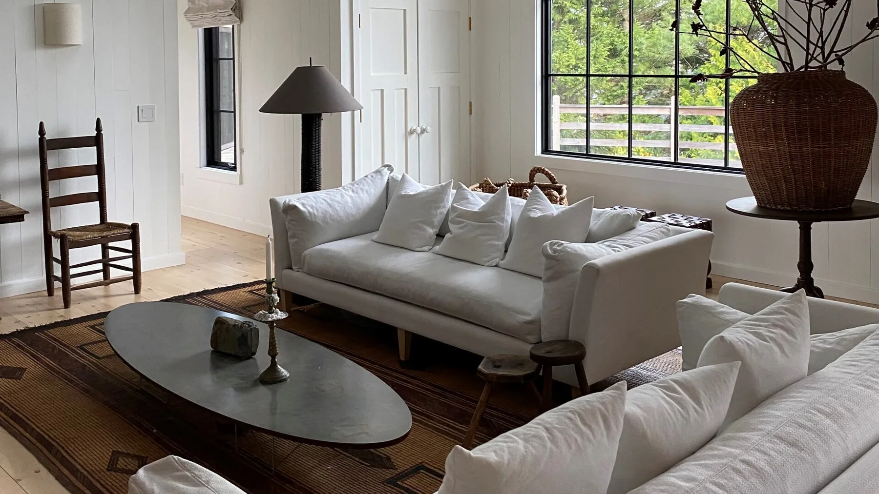 A bright living room with white seating, a dark coffee table, and large windows.