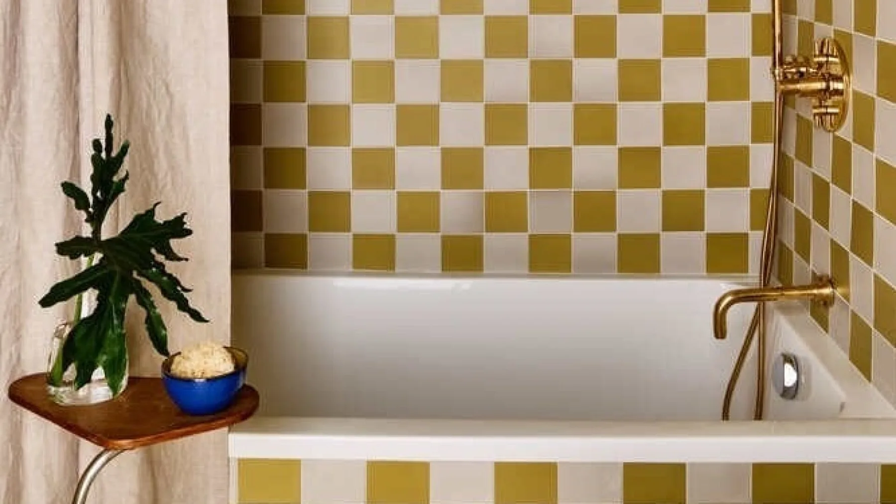 A bathroom with a bathtub, checkerboard tiles, and a small potted plant.