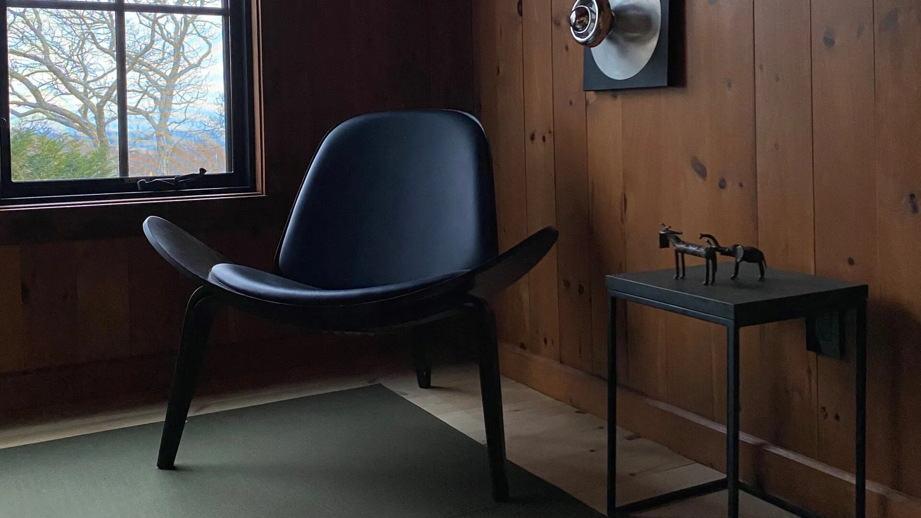 A wood-paneled room with a dark chair beside a small table and window.