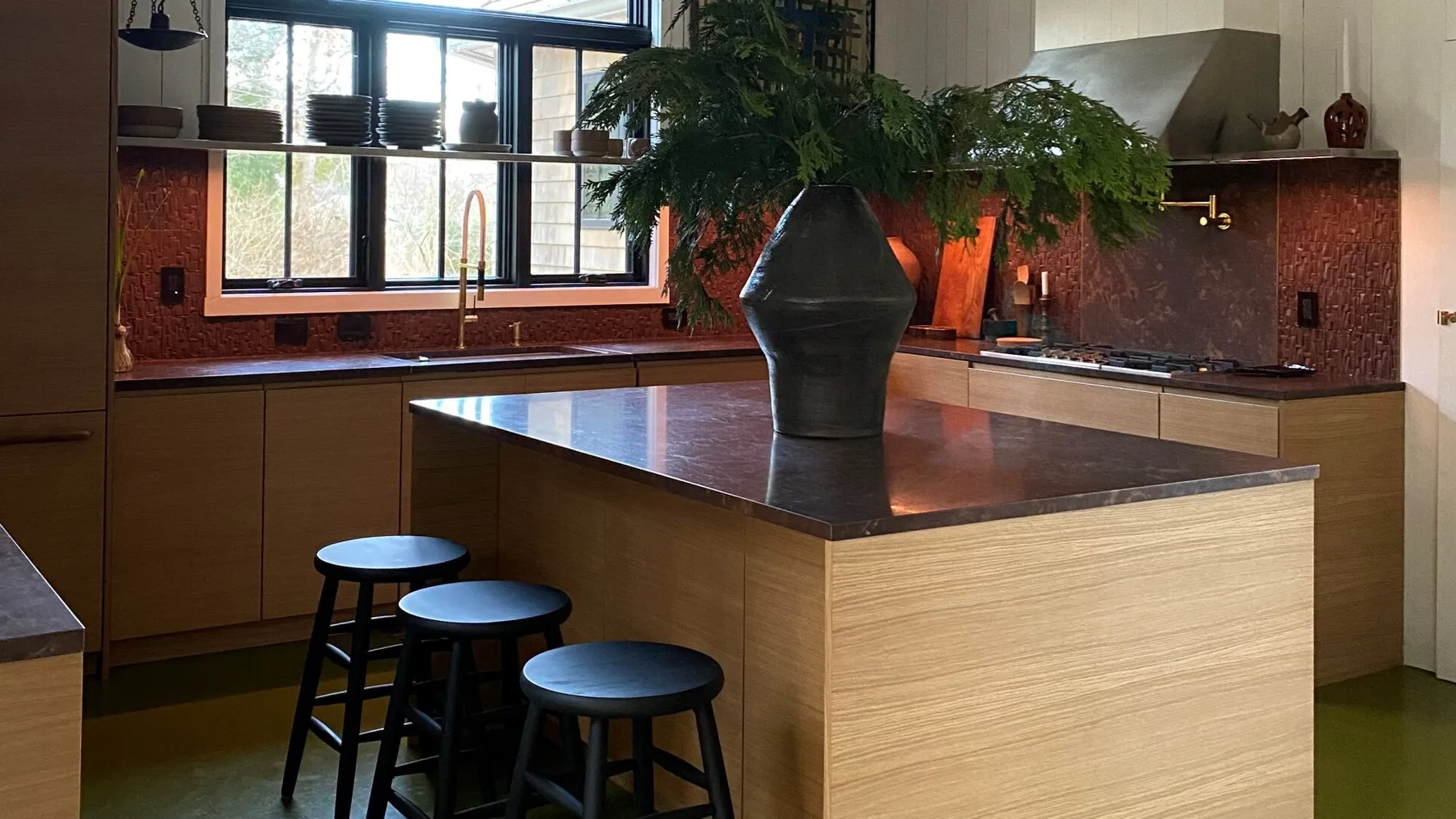 A kitchen with a central island, stools, and a large potted plant.