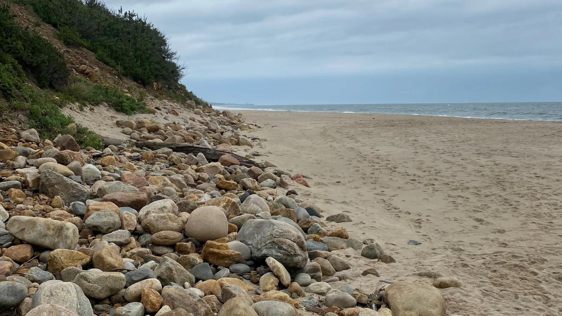 A sandy beach stretches beside a rocky shoreline under an overcast sky.