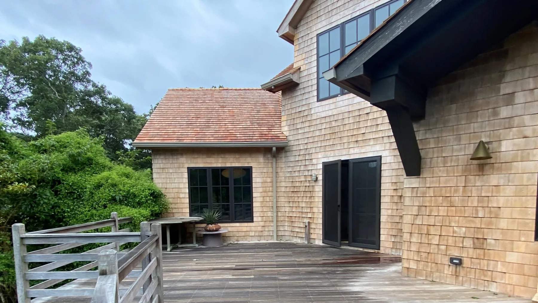 A wooden deck runs alongside a shingle-sided house with dark doors and windows.