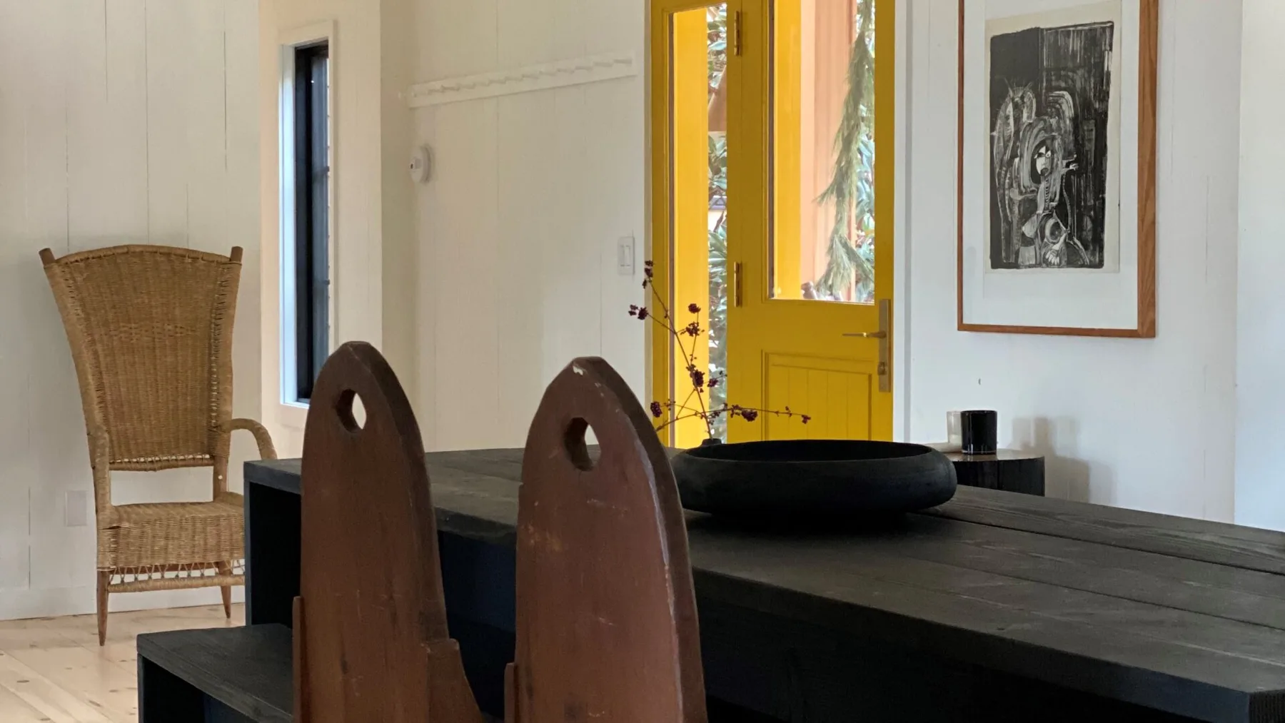 A dining area with a dark table, sculptural seating, and a bright yellow doorway.