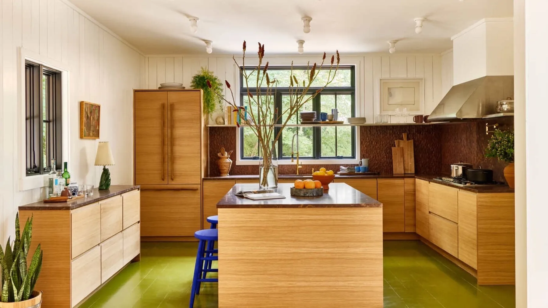 A bright kitchen with wooden cabinets, a central island, and green flooring.