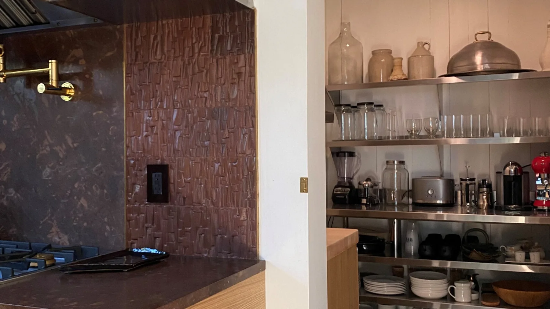 A kitchen with a stovetop and open shelves displaying dishes and cookware.