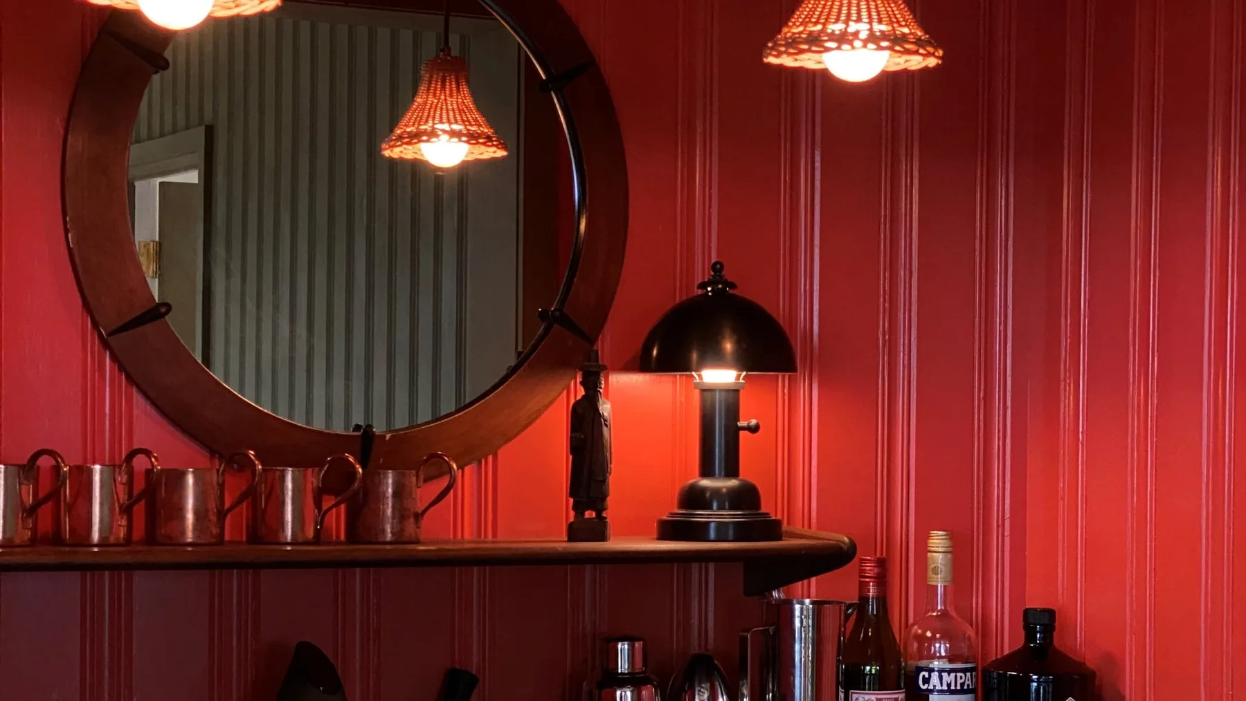 A red-walled bar area with a large round mirror and hanging lights.