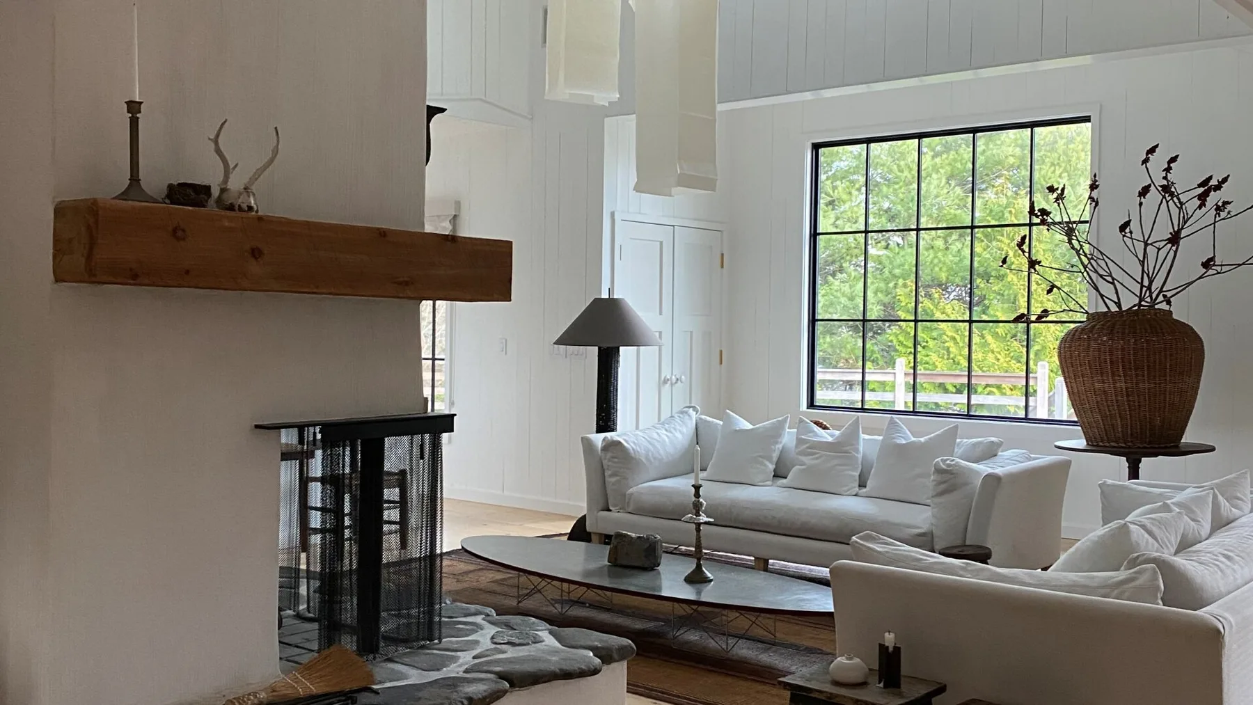 A bright living room with white seating around a fireplace and large window.