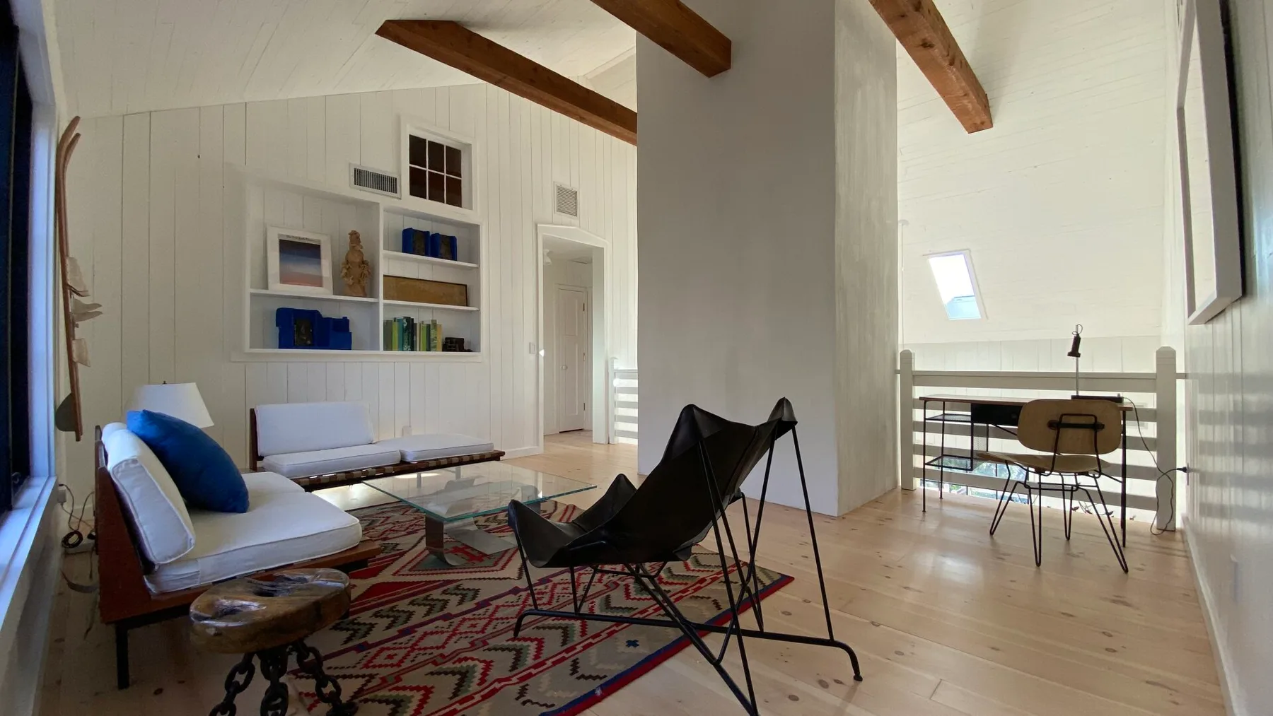 A bright living area with seating, a patterned rug, and exposed wooden beams.