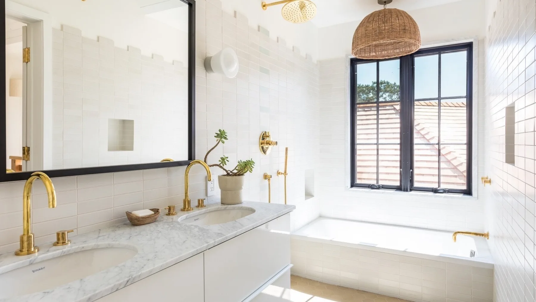A bright bathroom with a long vanity, large mirror, and bathtub beneath a window.