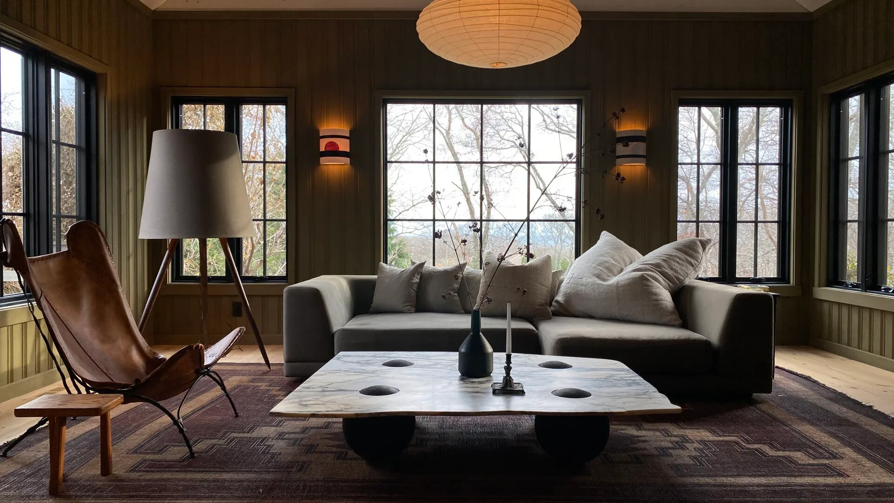 A living room with a sofa, lounge chair, and large central window.