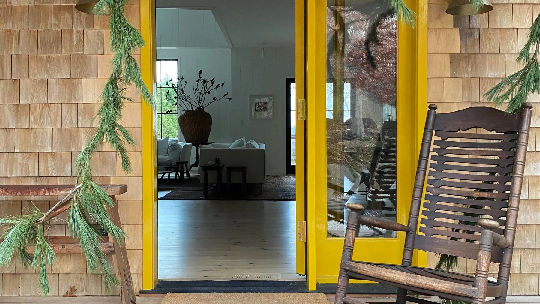 A wooden porch with a slatted rocking chair beside a yellow-framed glass door.