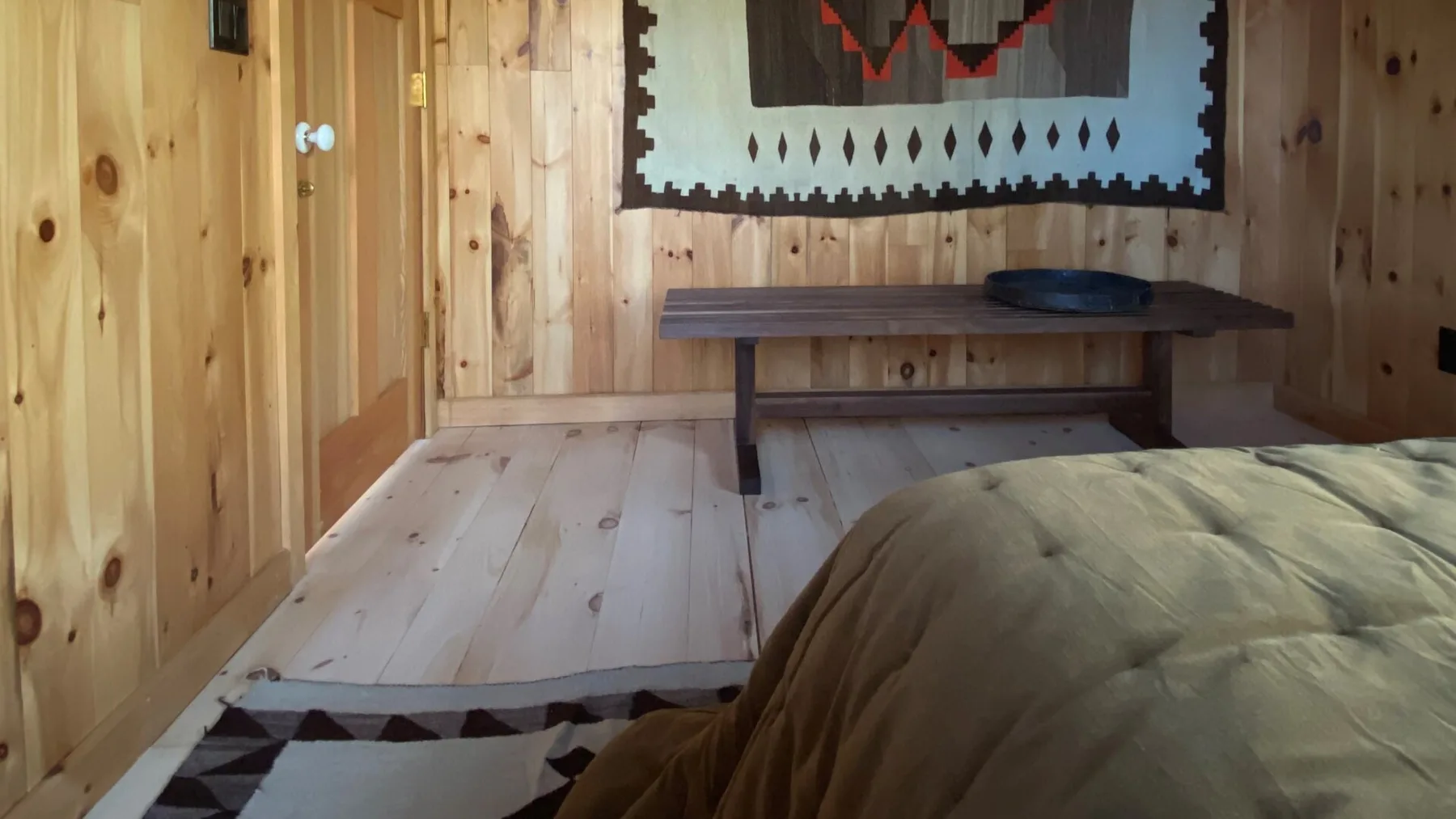 A wood-paneled room with a low table and a bed in the foreground.