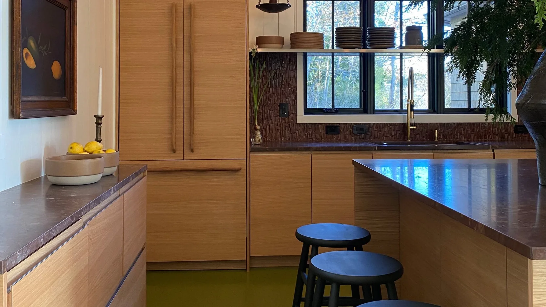 A modern kitchen with wooden cabinets, a central island, and windows overlooking greenery.