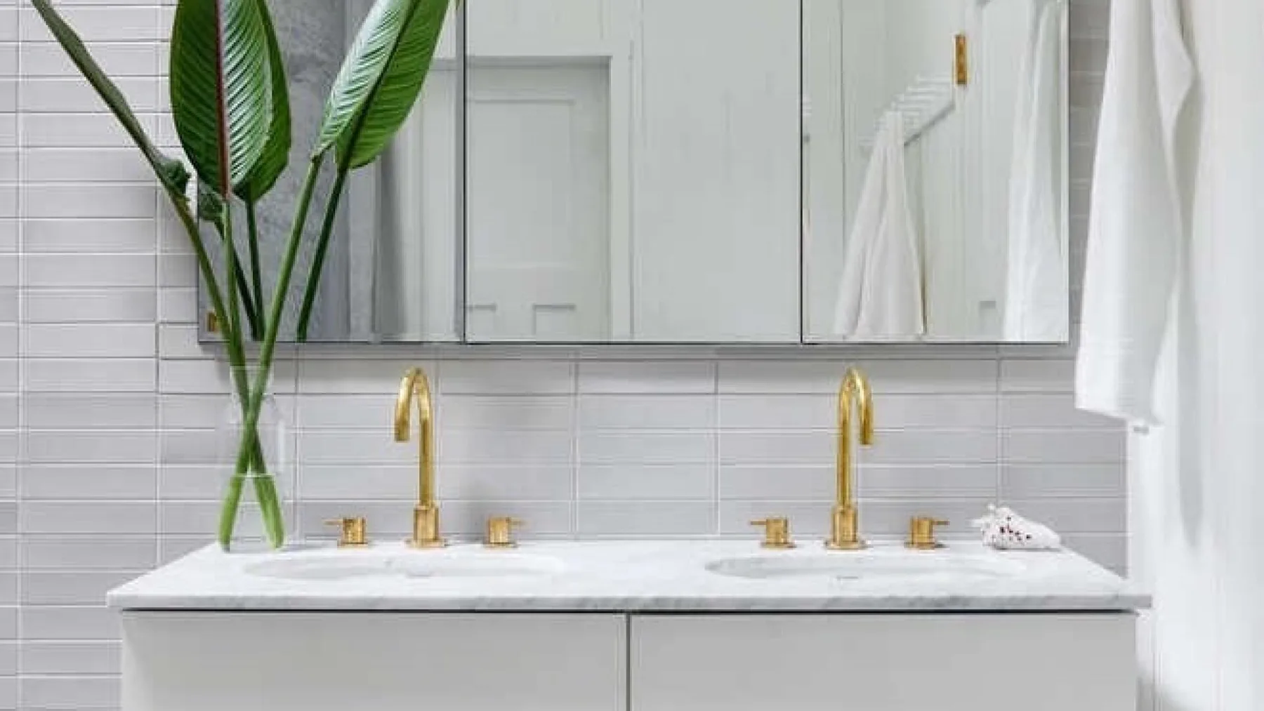 A bathroom vanity with two sinks, gold faucets, and a large mirror.