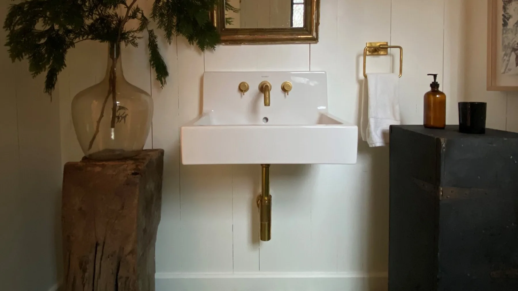 A bathroom sink with brass fixtures is set against a white tiled wall.