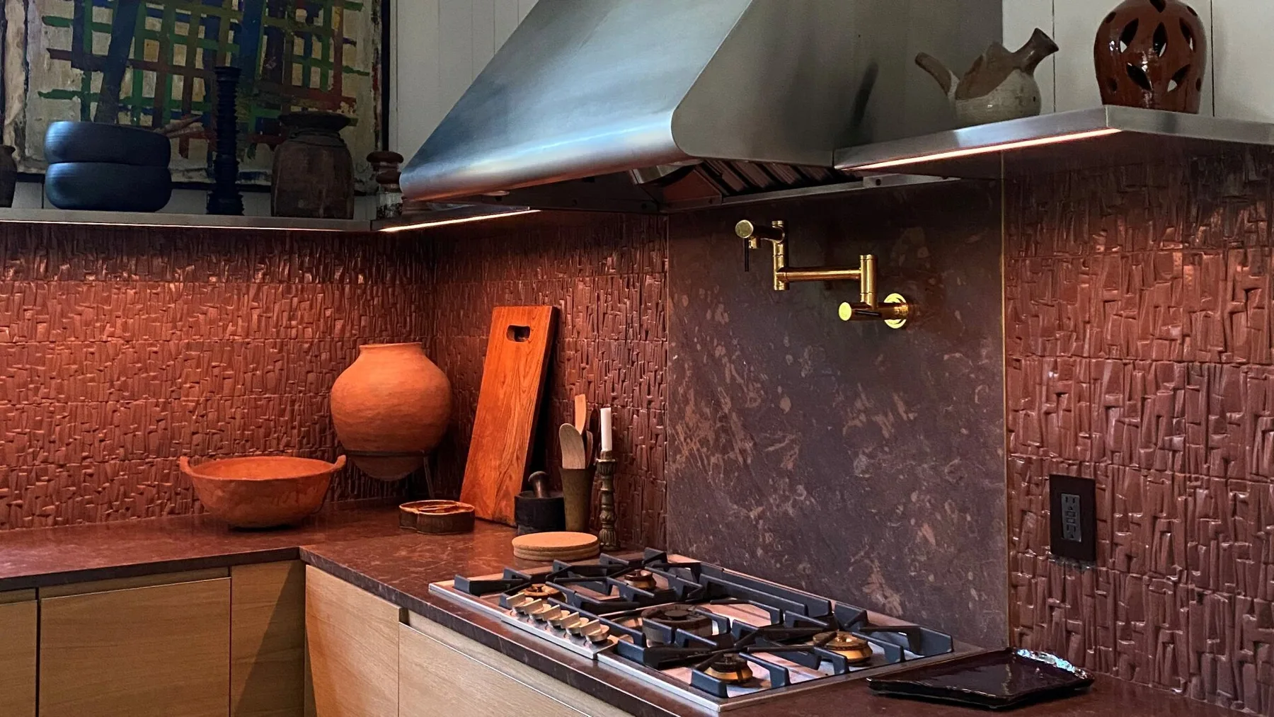 A kitchen cooking area with a gas cooktop beneath a metal range hood.