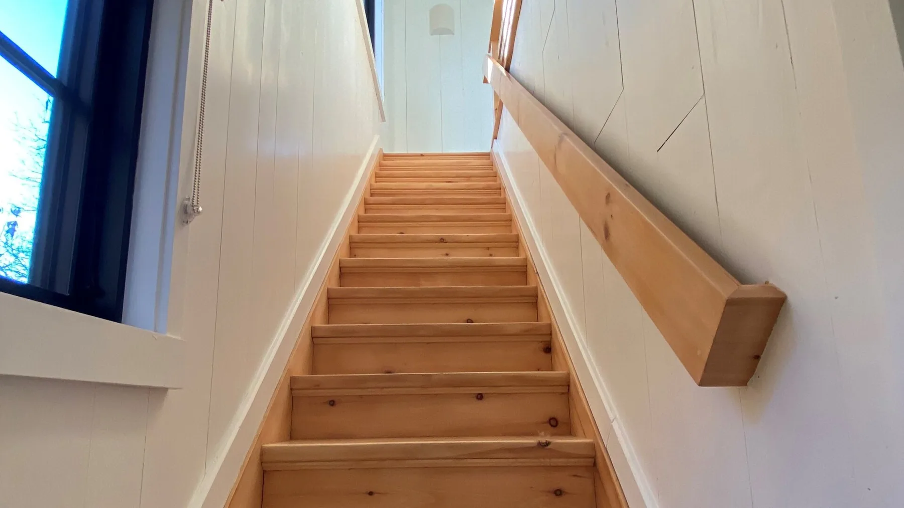 A wooden staircase rises between light-colored walls beside a window.