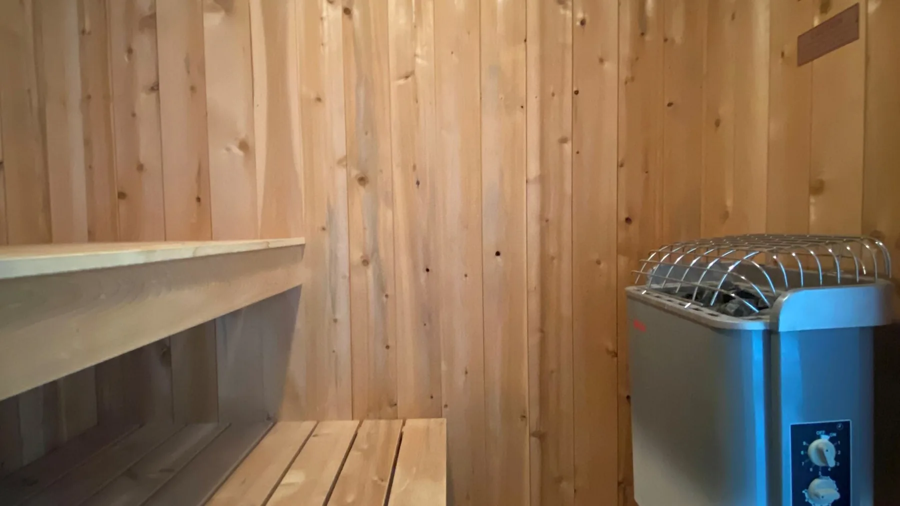 A wood-paneled room with a metal heater beside a wooden bench.