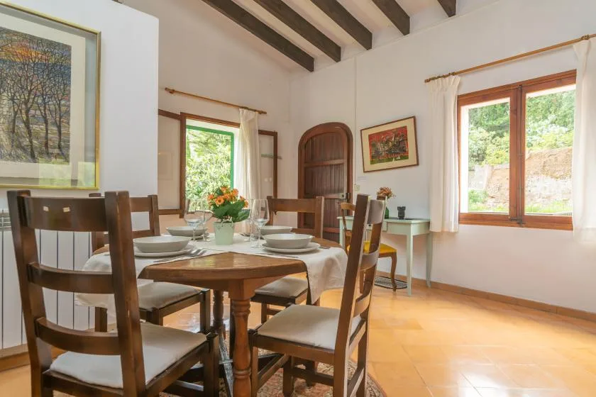 A dining room with a wooden table and chairs beneath exposed ceiling beams.