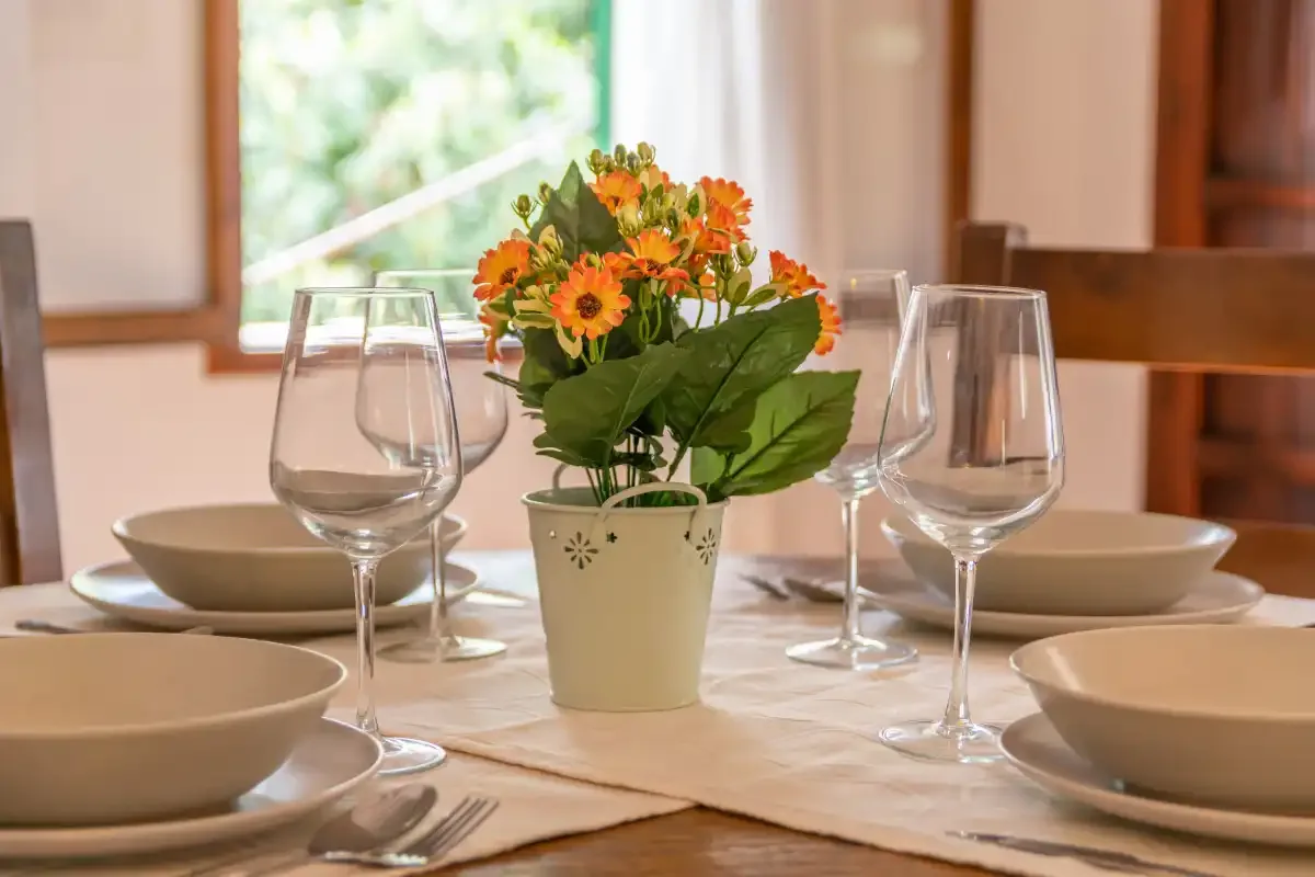 A dining table is set with dishes, glassware, and a flower arrangement.