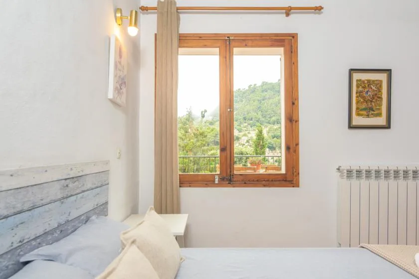 A bedroom with a wooden-framed window overlooking green hills.