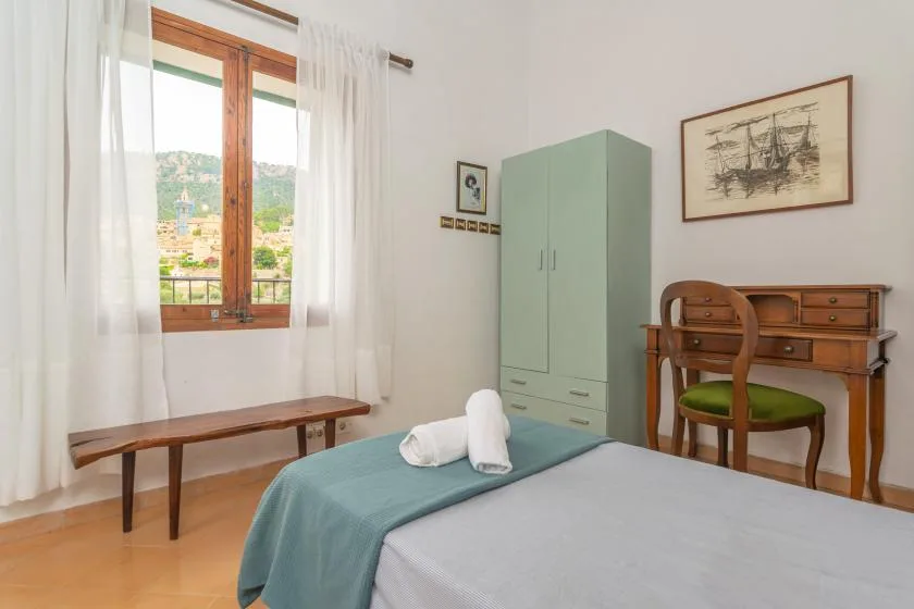 A bedroom with a bed, wooden desk, and window overlooking a hillside.