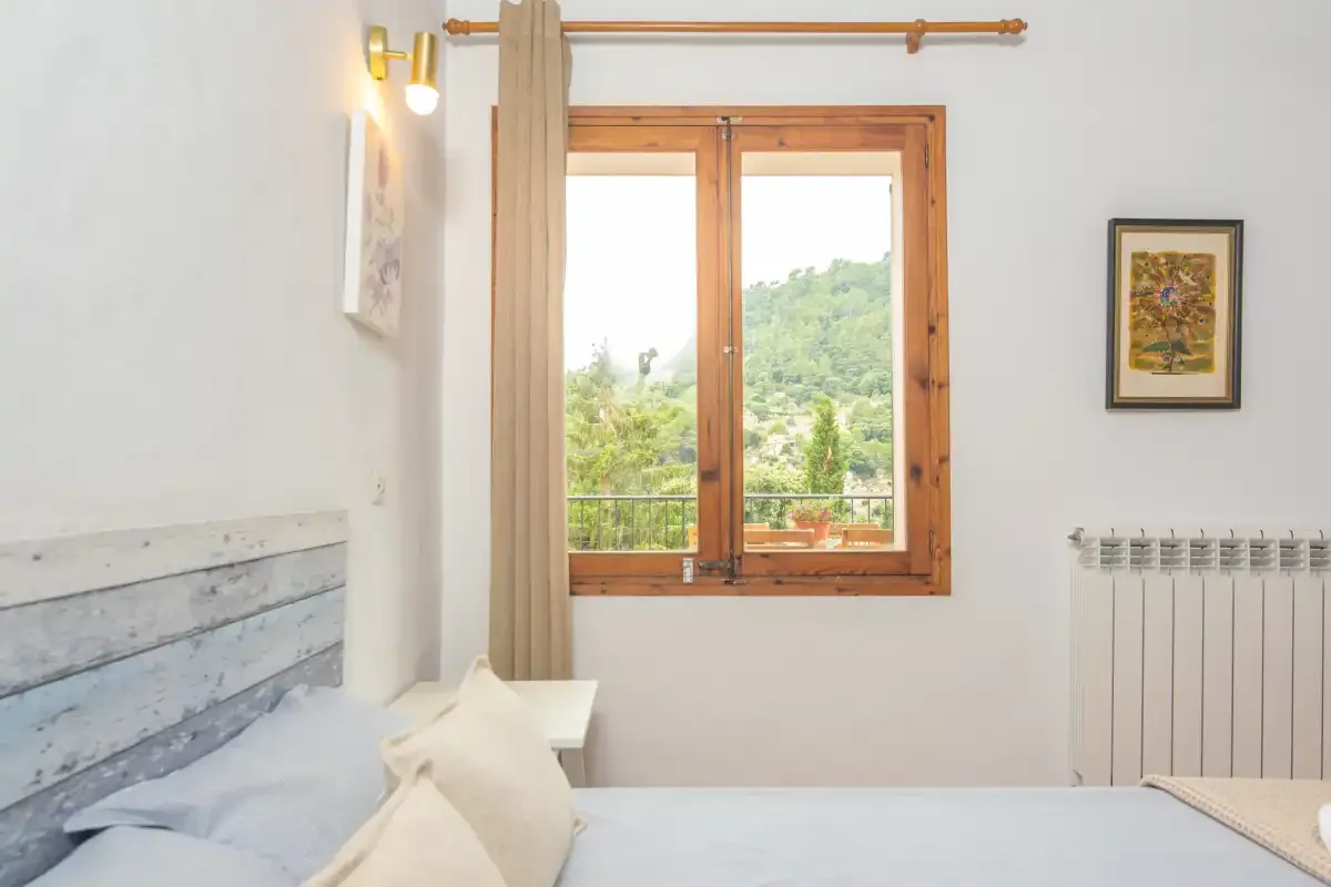 A bedroom with a wooden-framed window overlooking green hills.