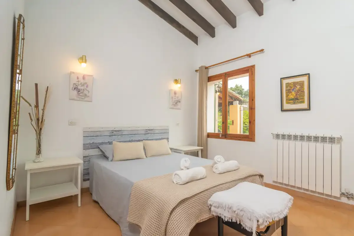Bedroom with a bed beneath exposed ceiling beams and a wooden-framed window.