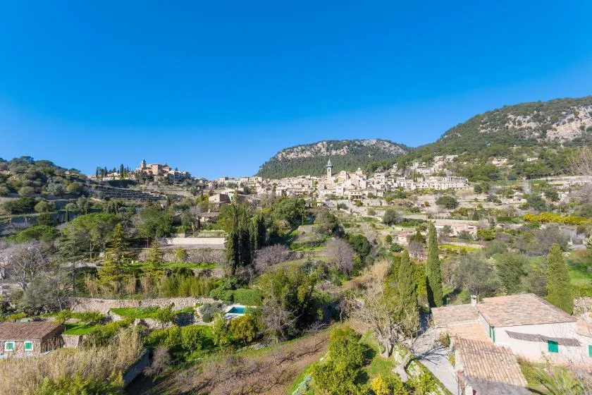 A hillside village sits among green vegetation beneath a clear blue sky.