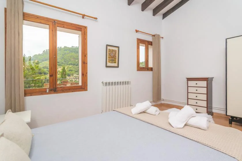 A bright bedroom with a bed, wooden-framed windows, and exposed ceiling beams.
