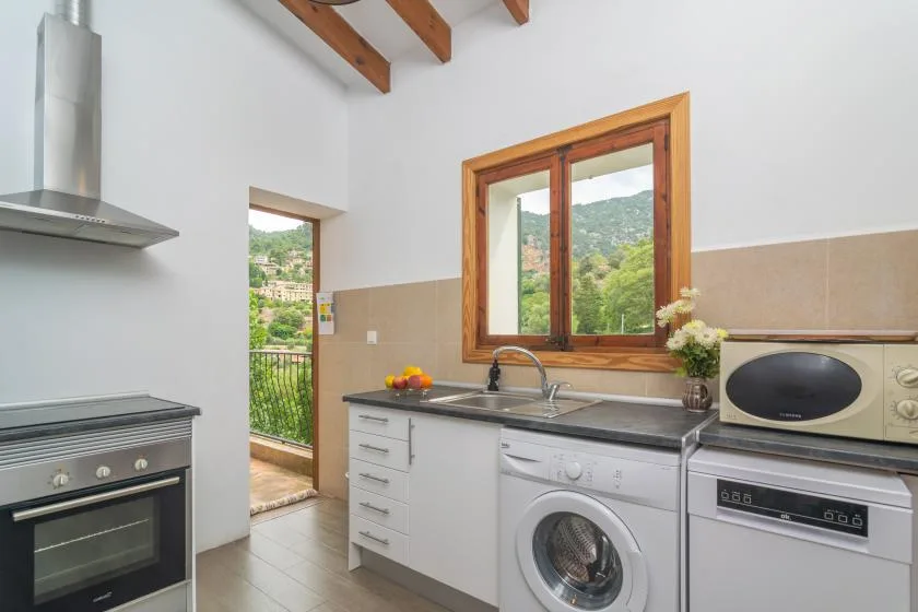 A bright kitchen with white cabinets, a sink, and a window overlooking green hills.