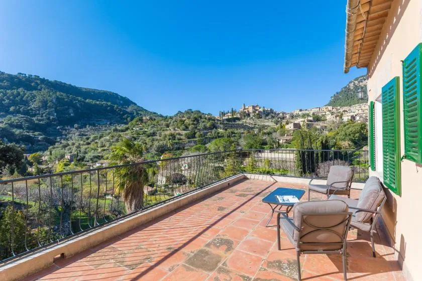 A sunny terrace with outdoor seating overlooks a green hillside.